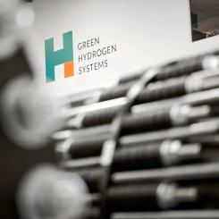 Green Hydrogen Systems' logotyp bakom elektrolysörstackar som är ur fokus. Foto: Green Hydrogen Systems.